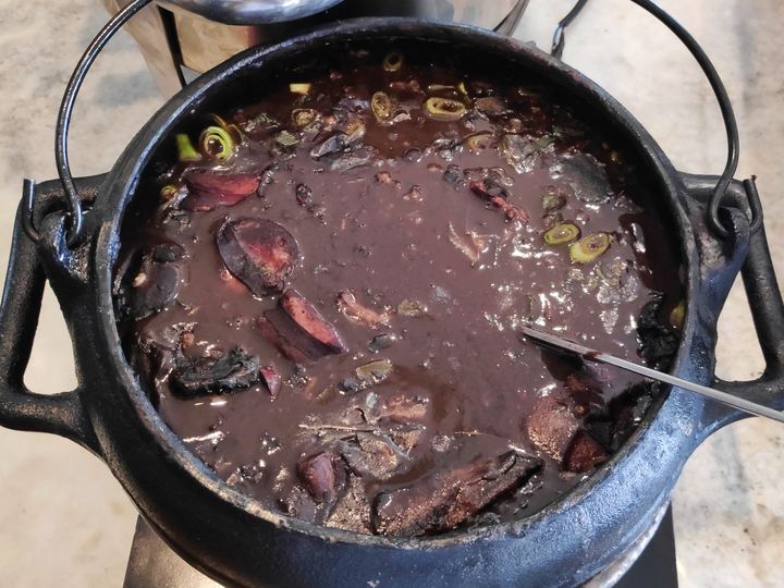 A black clay pot of feijoada with black beans, pork and sausage