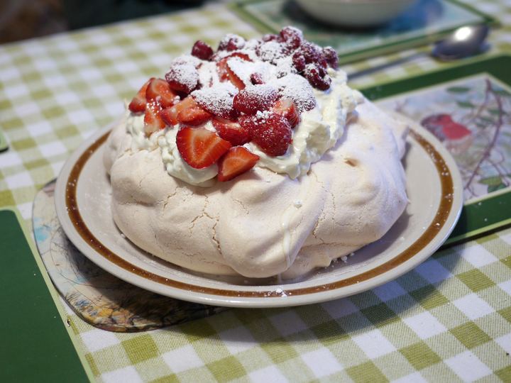 A pavlova topped with whipped cream, strawberries and raspberries