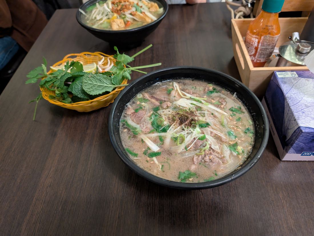 A bowl of beef pho with sliced beef, herbs and noodles